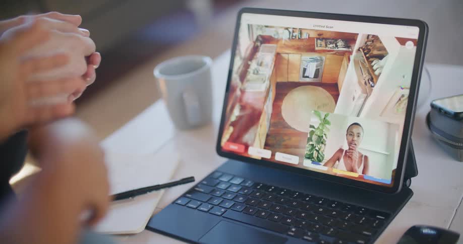 Two people in a room looking at a laptop on a table with a pen