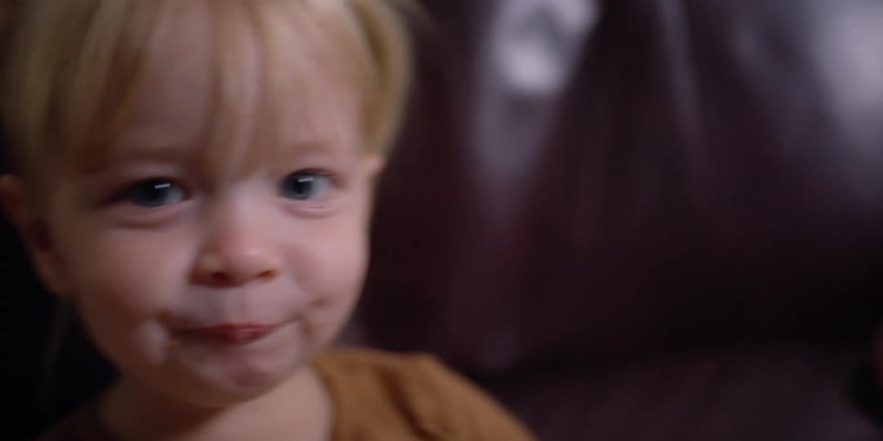 Grandmother with grey hair looks at blonde granddaughter sitting in armchair and eating food