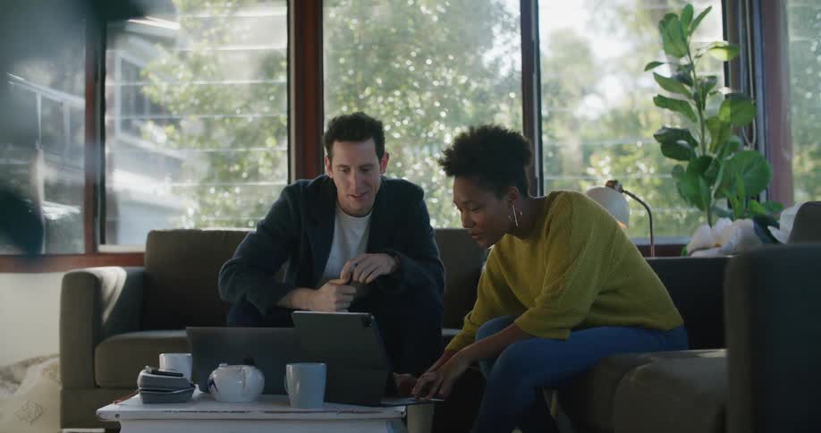 Coworkers are sitting on couches talking and pointing at laptops