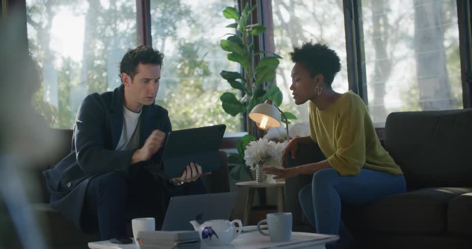 A man and a woman in a room sitting on a couch and looking at a laptop