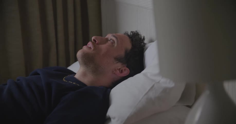 A man lying in bed runs his hands along his face before sitting up