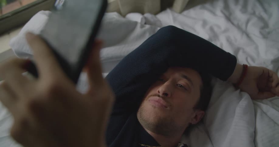 Man checks his cell phone and shakes his head while laying in bed