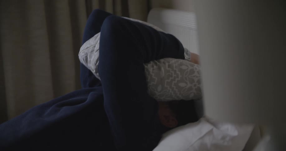 A man laying in the bed tosses his cell phone