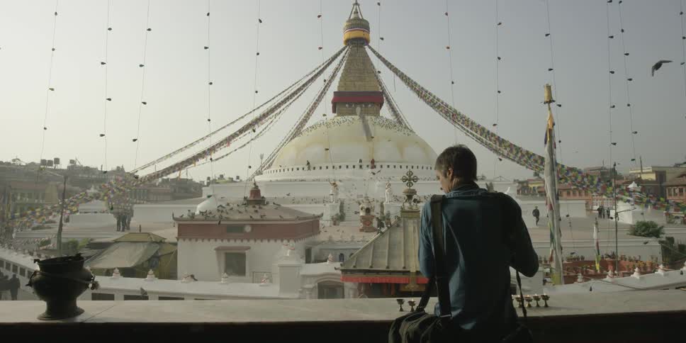 A photographer takes pictures of a buddhist temple with pigeons sitting on the roof