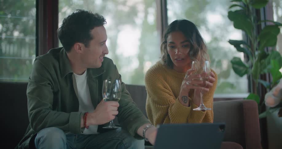 Man with green shirt and woman wearing yellow sweater hold wine glass and talk with each other