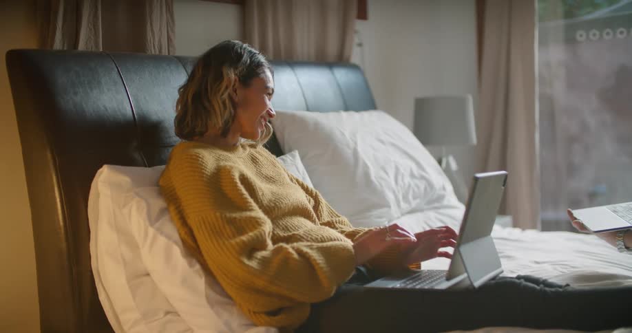 A man and woman using laptops laying in a bed