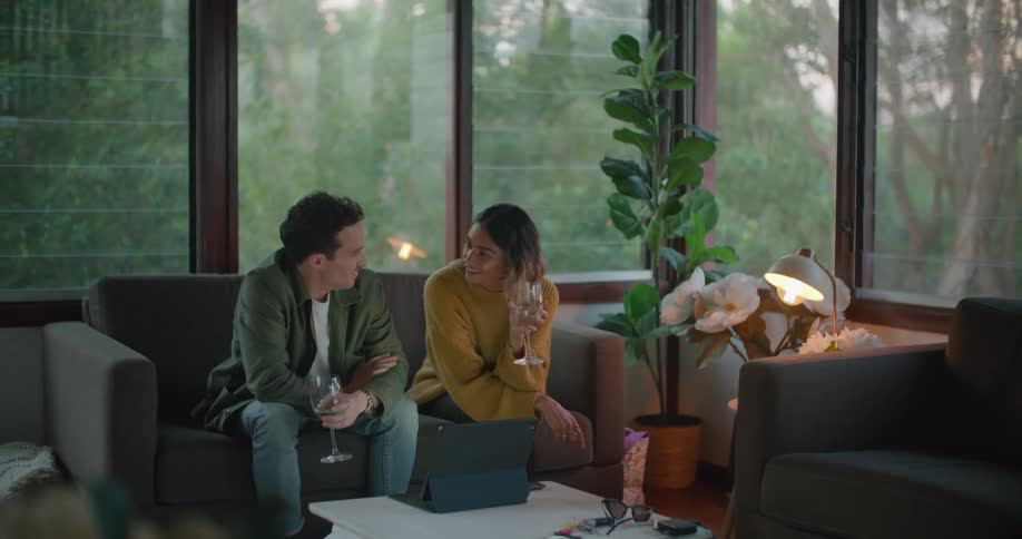 A man and woman drink wine while sitting on the couch in front of a laptop