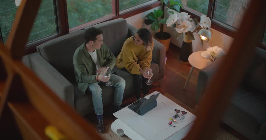 A young man and woman sit together indoors while drinking wine and chatting