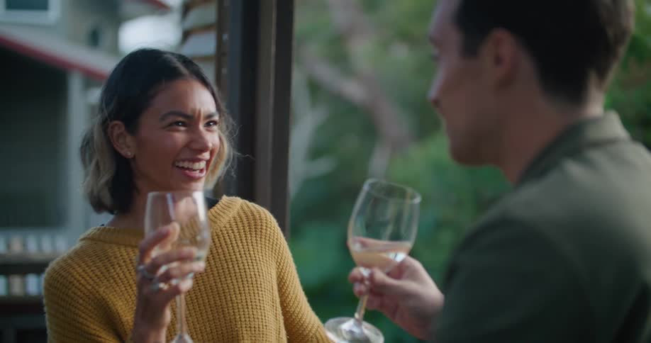 A man and woman laugh while chatting and drinking wine outdoors