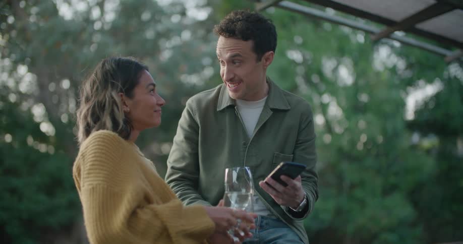 Man holds a cell phone while he and a woman hold wine glasses