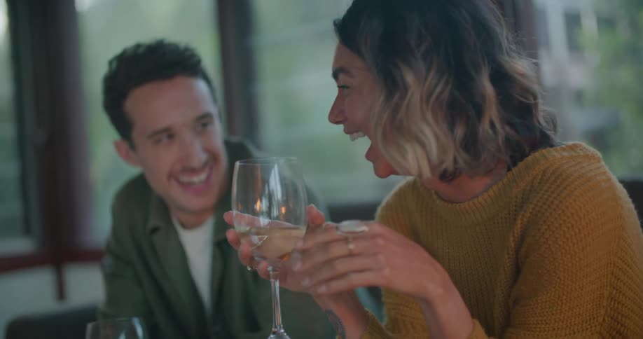 Man and woman holding wine glasses smile and gesture while talking