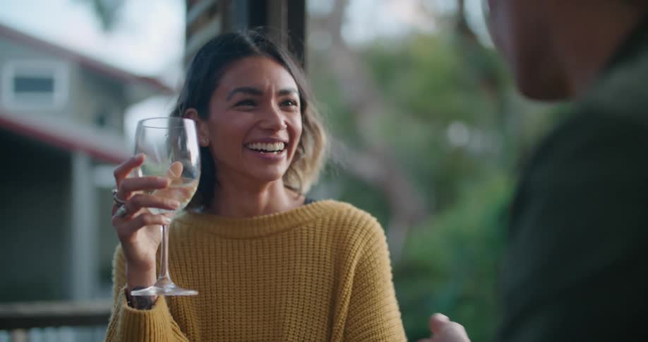 Woman with yellow sweater holds up wine glass and listens to man talking to her laughing