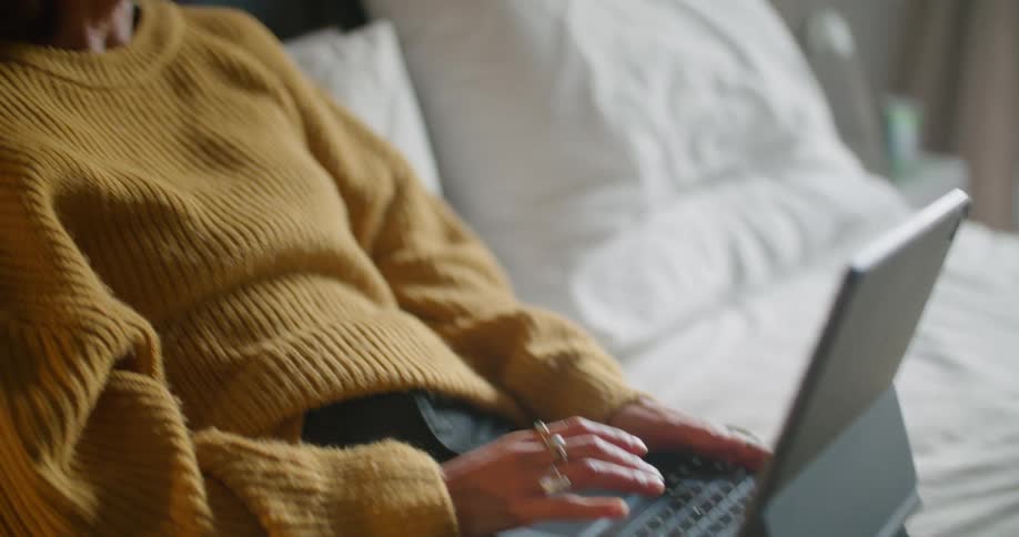 A man and a woman in a room sitting on a bed looking at laptops