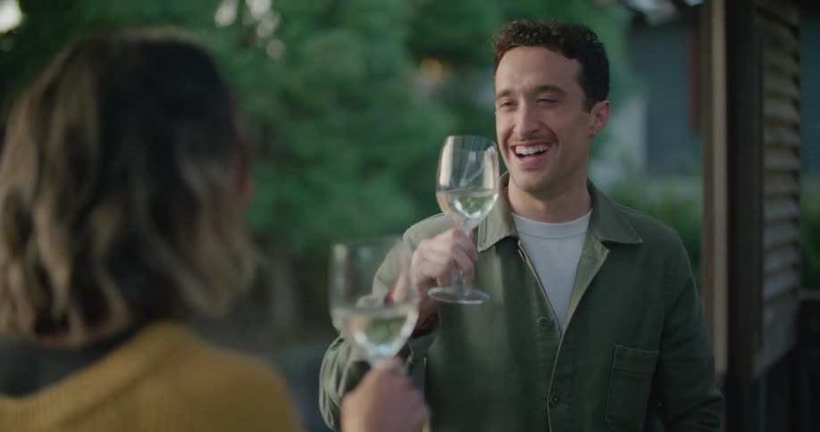 Man and woman smile and laugh as they make a toast with their wine glasses then drink the wine