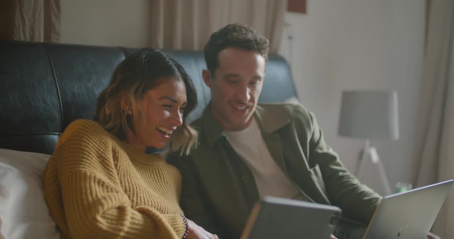 A man and woman sit beside each other laughing with laptops in front of them