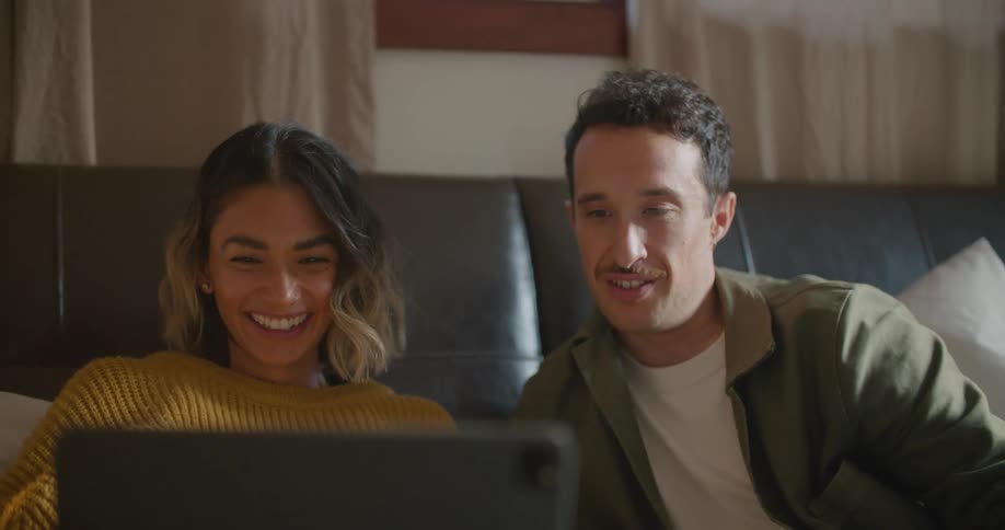 Man and woman sit on a sofa and laugh as they look at a laptop screen