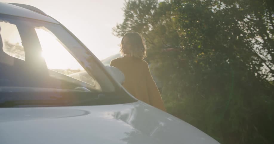 Woman gets out of car and walks down drive way smiling at man carrying box as traffic passes on nearby street