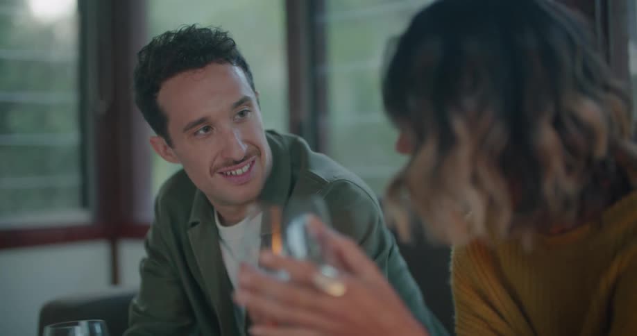 A man and woman sit together on couch while talking and drinking wine
