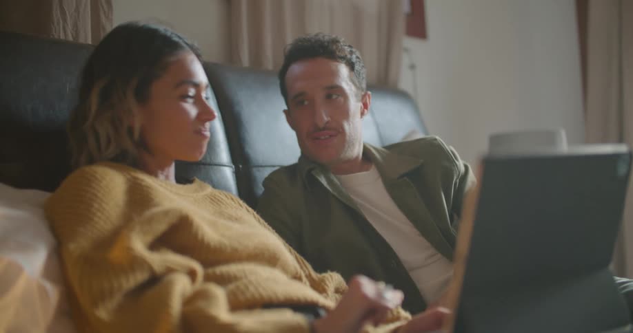 A man and a woman in a room laying on a bed looking at a laptop