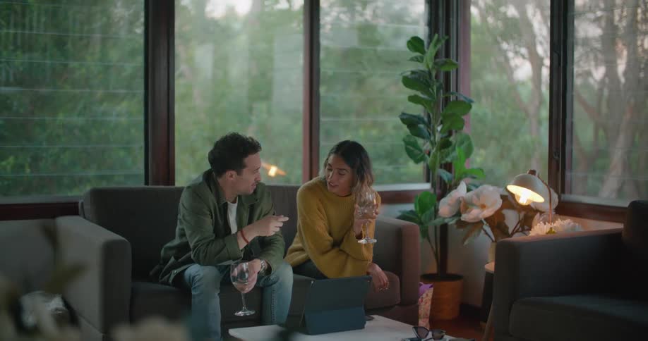 A couple are talking while sitting on a couch as they drink white wine