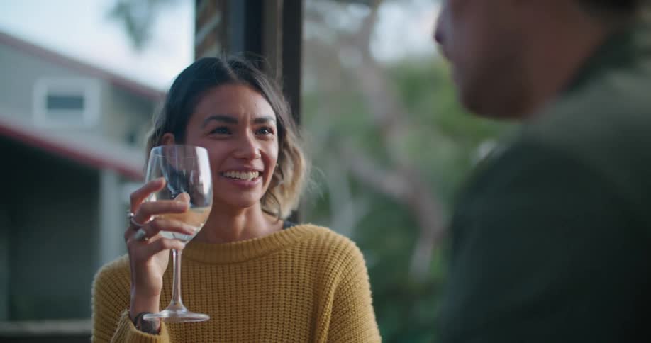 A woman holding a large wine glass smiles and laughs while listening to her male companion speak