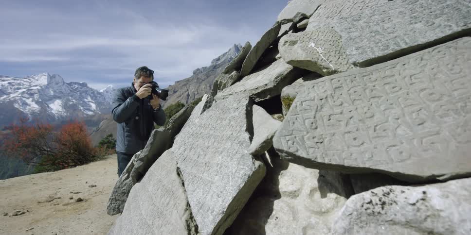 A man photographs a pile of stone covered with carvings