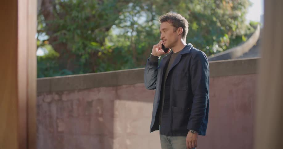 Man with dark jacket and jeans talks on smartphone and hangs up