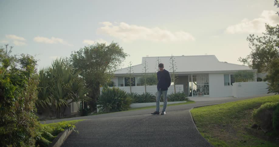 A man standing in a driveway with a house trees the sky and clouds in the background