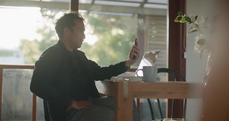 A man is sitting at a table and talking on a cell phone
