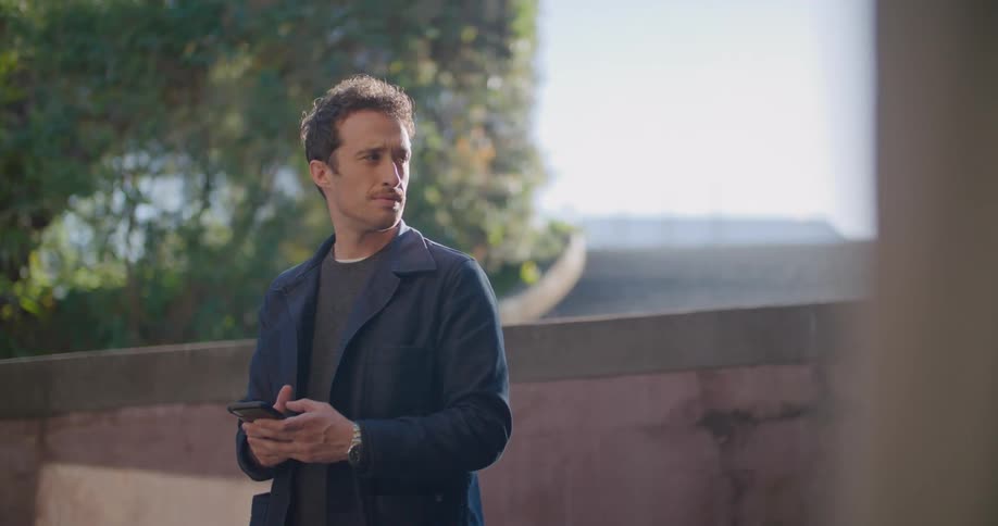 Man standing near fence types on mobile phone as car passes by in background