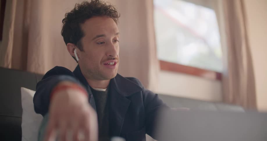 Man with dark jacket and earphones makes a video call on laptop
