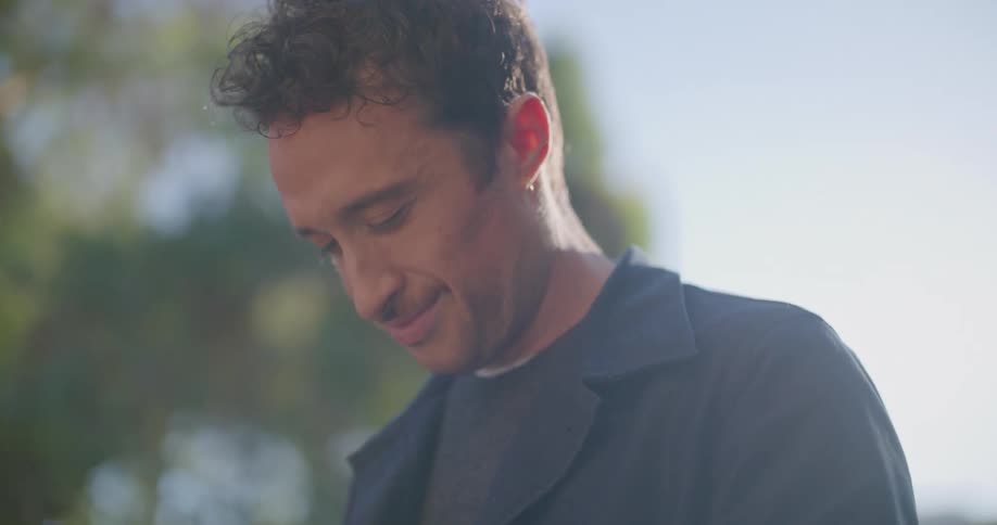 A man smiles while typing outside on his smart phone