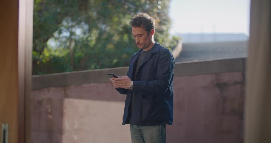 Man types with his thumbs on his cell phone as a car passes by behind him