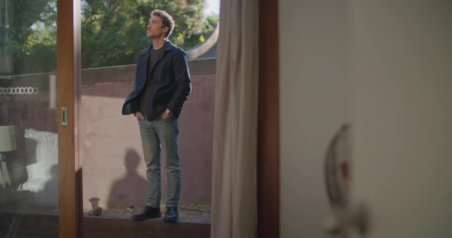 Man stands outside near wall looking around with his hands in his pockets