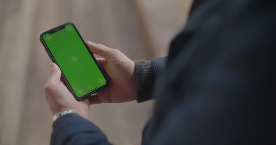 Man wearing coat holds and views mobile phone