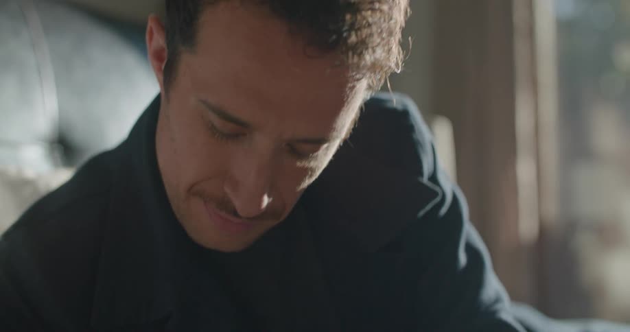 A man in a room laying on a bed writing in a book with a pen