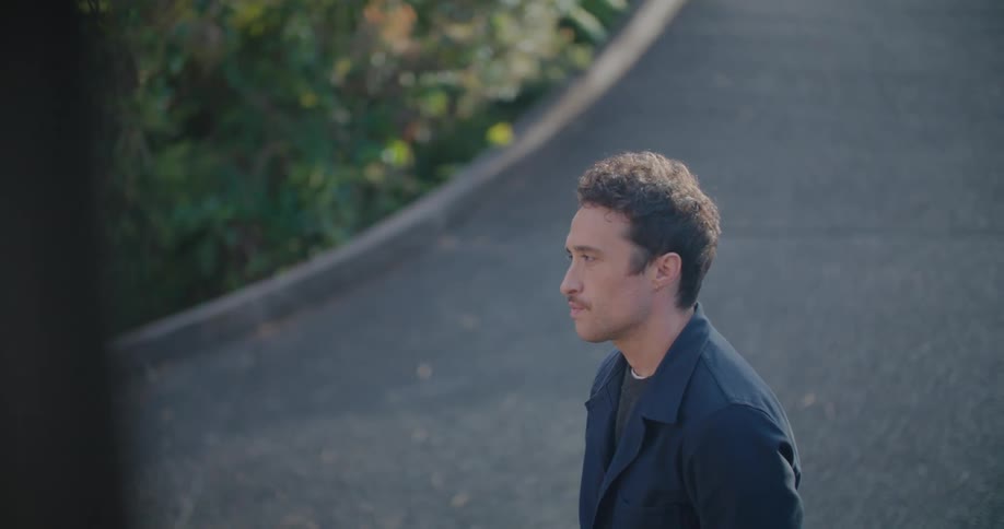A man standing on a pathway with plants and leaves in the background
