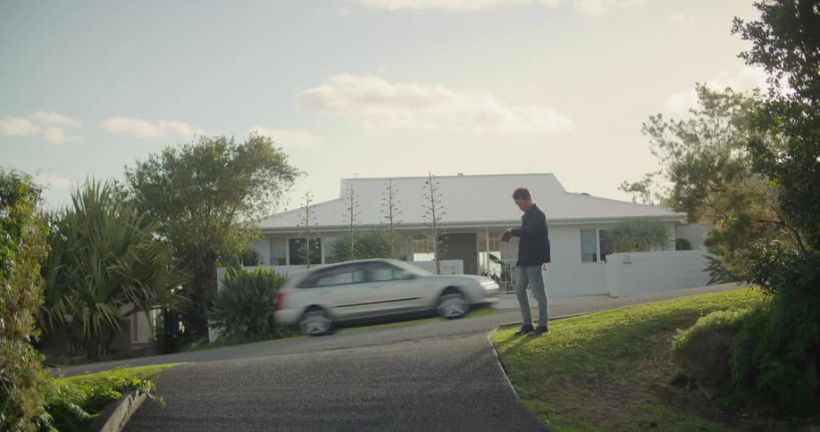Man stands near driveway road intersection waiting as vehicles pass by