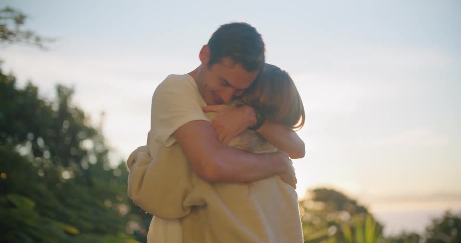 A man and a woman hugging with trees the sky and clouds in the background