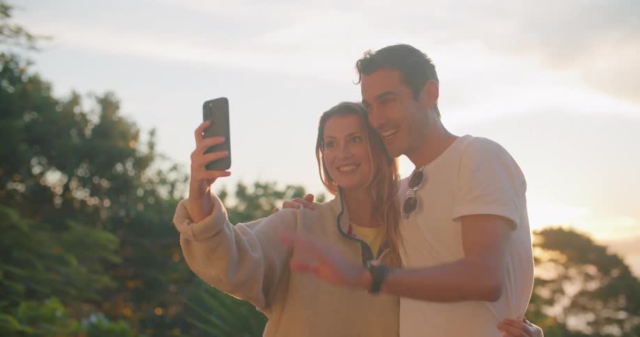 A woman and man embrace as the woman takes a photograph of themselves with her smartphone