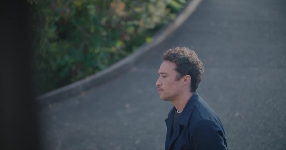 A man purses his lips and looks around while standing near his driveway