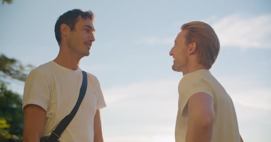 Two male friends approach each other and smile and hug on a sunny day