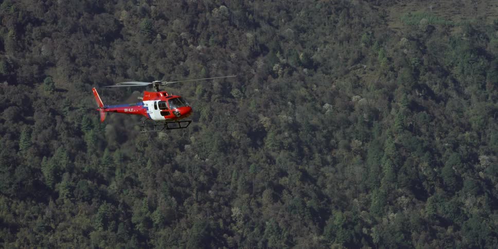 A red and white helicopter flies over a forest