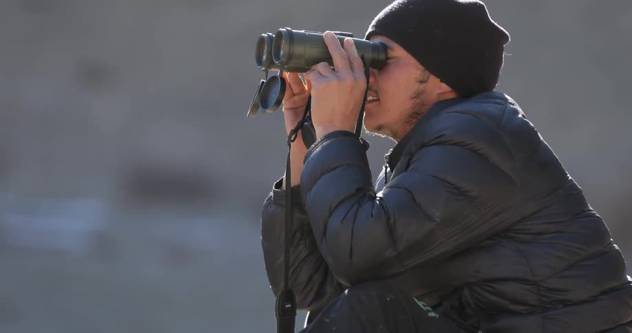 A man looks through then adjusts binoculars
