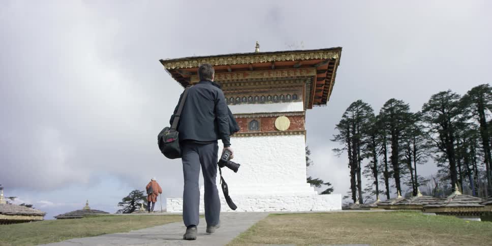 A photographer walks towards a building on a cloudy day