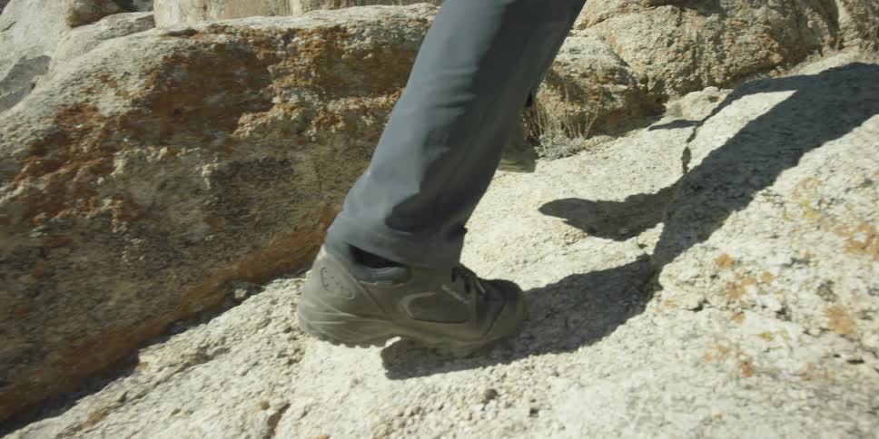 A person walks up a rocky hill on a sunny day