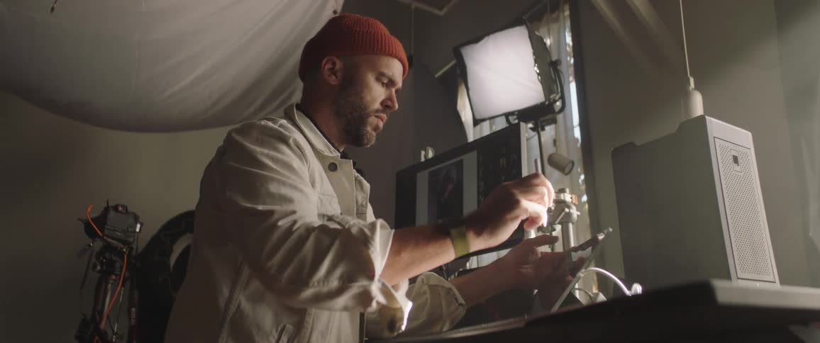 A man in a photography studio uses a stylus while operating a tablet on a computer desk