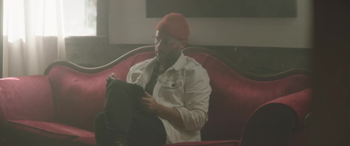 Man with a red woolly hat and a white jacket sits on a red couch and uses a tablet
