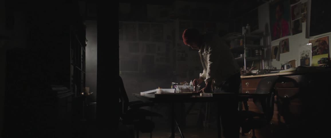 Man standing in front of a low table in a dark room sketching