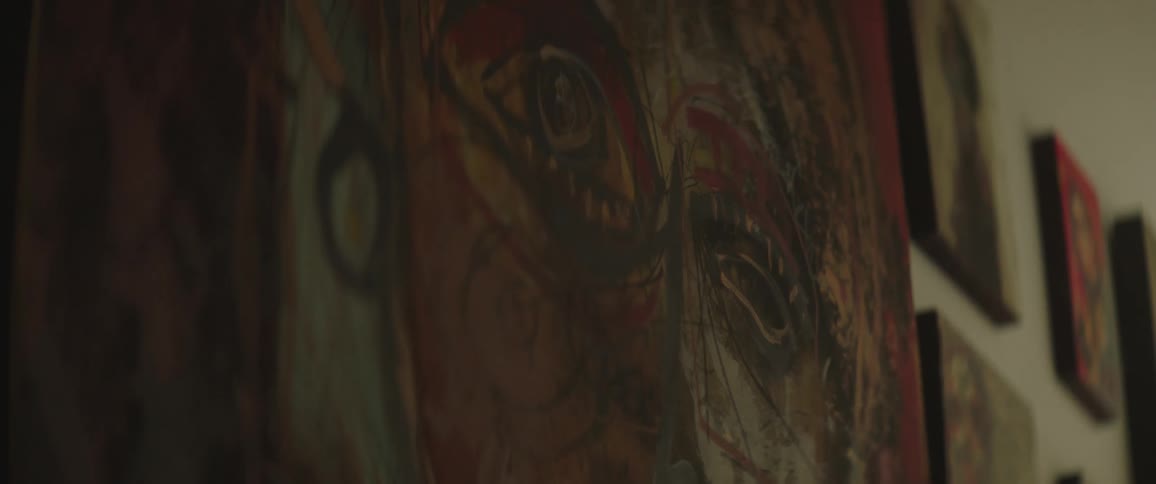 Canvas of painted face using reds and browns hangs on wall with other art